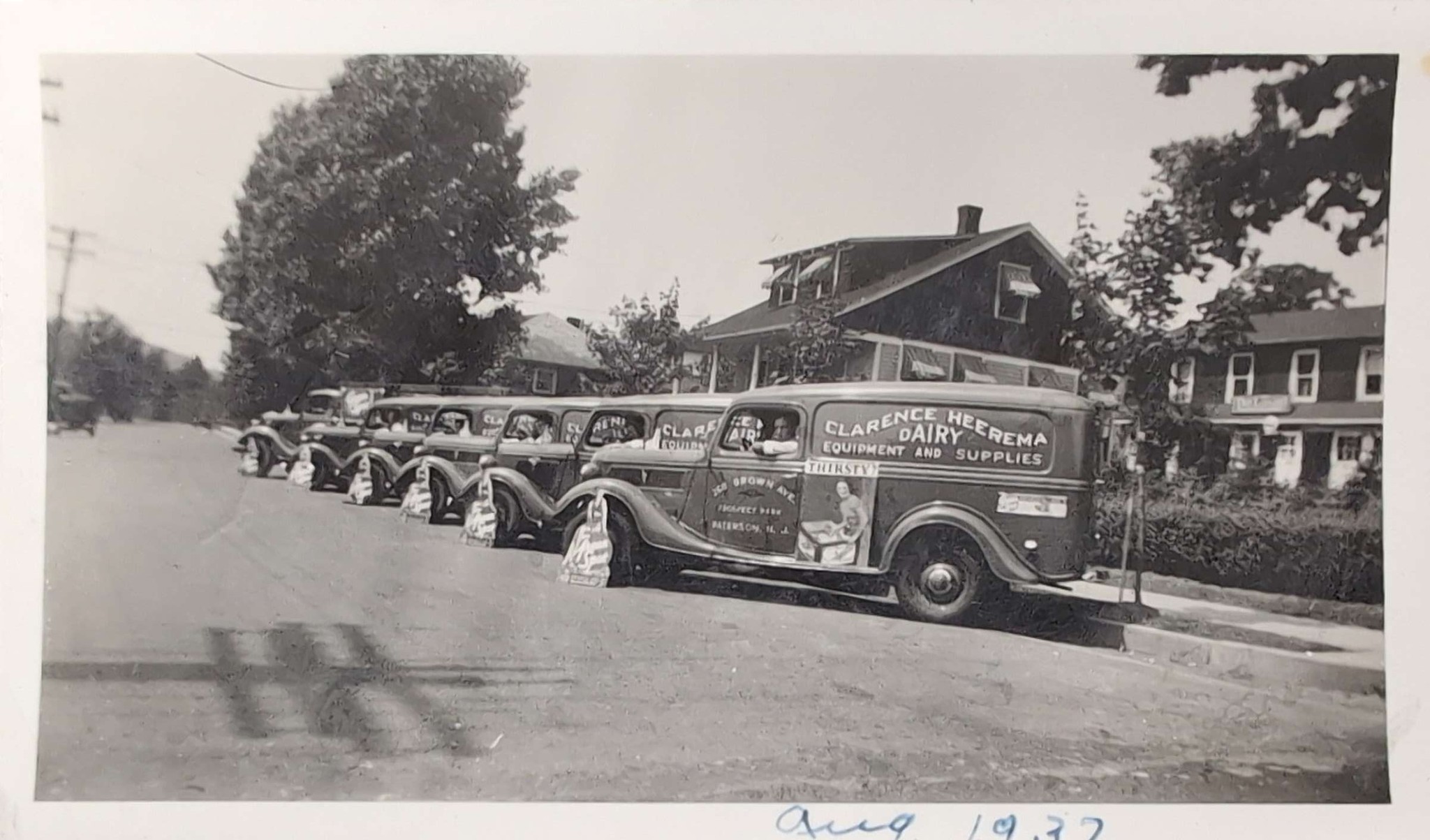 Fleet of vintage Clarence Heerema Dairy Equipment and Supplies trucks lined up on a residential street in Paterson, New Jersey in August 1937.