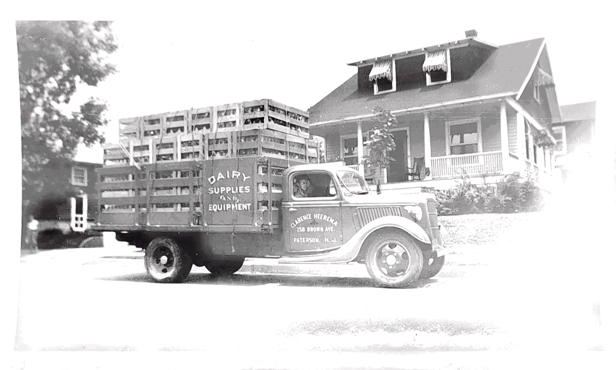 An early Clarence Heerema Dairy Supplies and Equipment flatbed truck loaded with wooden crates outside the company founder's home.